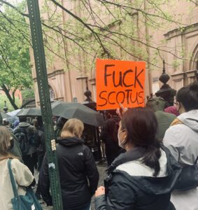 A group on the street protests the leaked memo overturning Roe v. Wade. One protester holds an orange sign that reads 'Fuck Scotus'