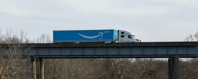 Blue tractor trailer with Amazon Prime logo crosses a bridge over water.