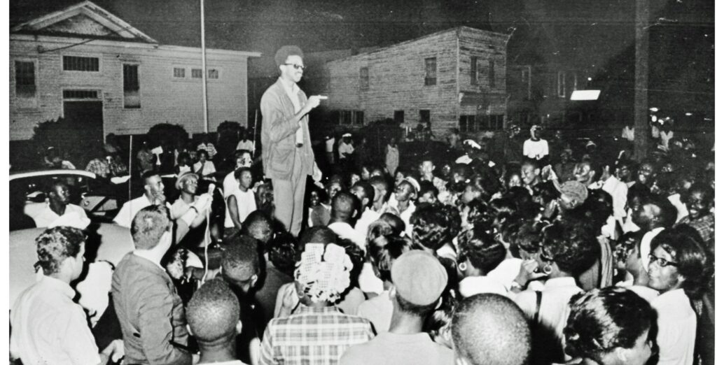 H. “Rap” Brown stands atop a car in the African American section of Cambridge, Md., July 24, 1967 delivering a fiery black nationalist speech denouncing white dominated society and urging African Americans to fight back. Later that night, Brown was wounded by shotgun pellets before he left town. In the early morning hours, someone set fire to an African American school that ended up burning two square blocks while the town’s firemen stood by. Maryland Gov. Spiro T Agnew immediately denounced Brown and he was soon charged with inciting to riot, along with other crimes. The National Guard was again called out to occupy the town. Brown faced other legal woes, but charges in the Maryland case were ultimately dropped several years later. The incident marked the end of the mass civil rights movement in Cambridge that began in 1962. Photo Credit; Washington Area Spark (https://www.flickr.com/photos/washington_area_spark/49222107273/in/album-72157702777400382/)