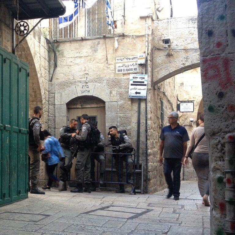 Temple Mount Israeli checkpoint at the corner of al-Wad St. (looking south) & Bab el-Hadid Rd. (to the left/east), Old City of Jerusalem. The arch's inscription says Beit Elhanan (בית אלחנן), “Elhanan House”. Photo Credit: Jj M Ḥtp via Wikimedia.