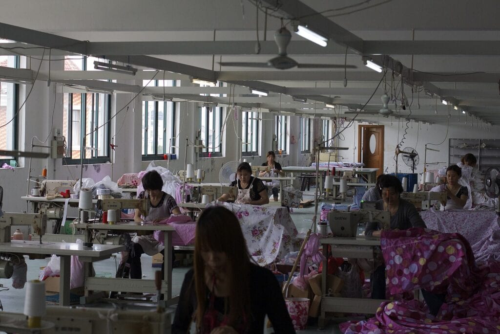 Poorly lit, partly empty silk factory with tired looking women hunched over their work.