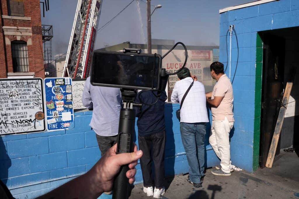 Onlookers watch a fire destroy the Lucky Ave Wholesale Center in Downtown LA, June 19, 2025. The federal campaign to deport undocumented immigrants in Los Angeles began in early June when ICE agents arrested workers at a nearby garment factory.