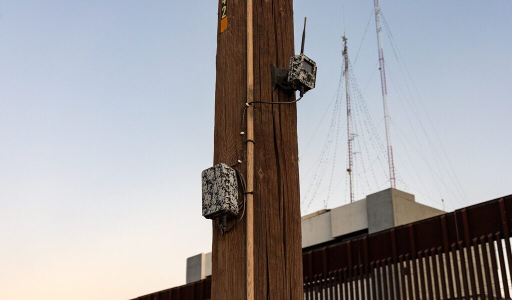 Remote camera on a pole with landing mat- and bollard-style border fencing in the background at the US/Mexico border in Calexico, California. Photo Credit: Dugan Meyer