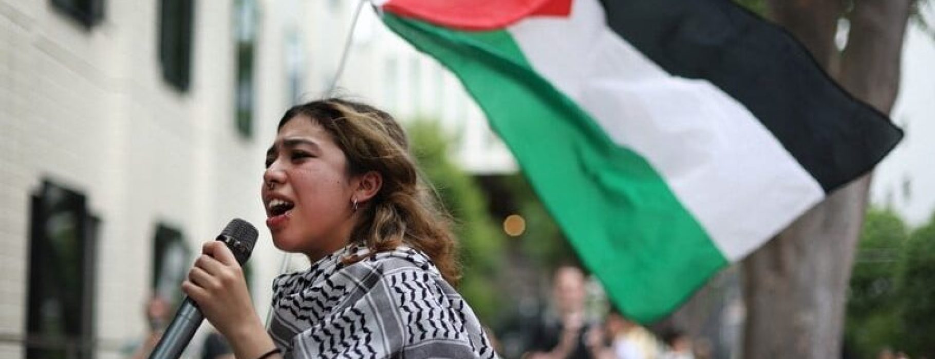 9 Kasemu Juman is seen speaking into a microphone as she holds a Palestinian flag at Sophia University in Tokyo's Chiyoda Ward on May 30, 2024. (Mainichi/Yoshiya Goto)