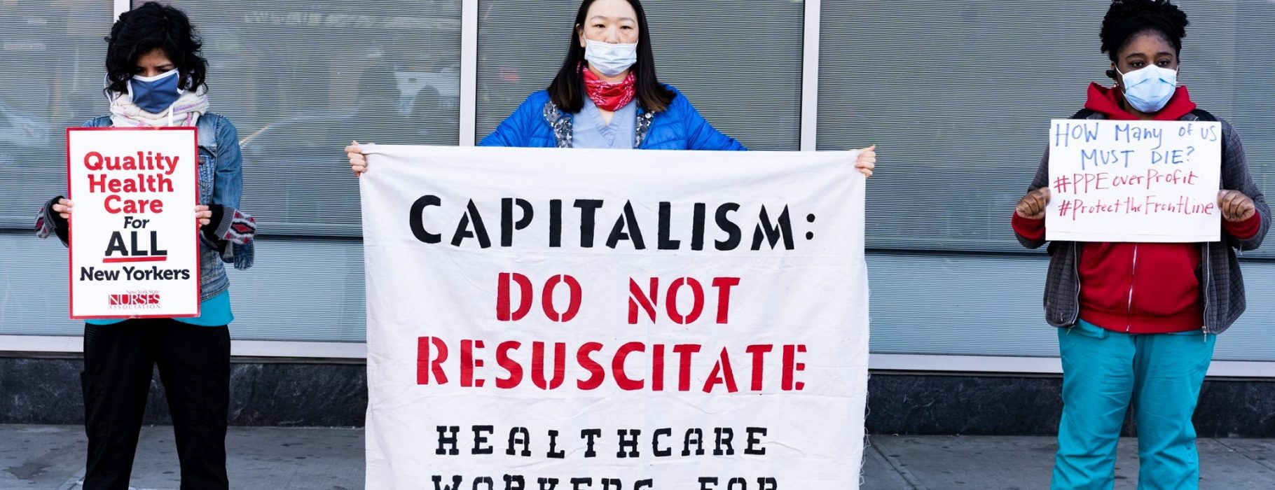 Healthcare workers in masks hold up three protest signs and banners: Quality Health Care for All New Yorkers, Captialism: Do Not Resucitate: Healthcare Workers for Socialism, How Many of us must die? #PPEoverprofit #ProtecttheFrontLine