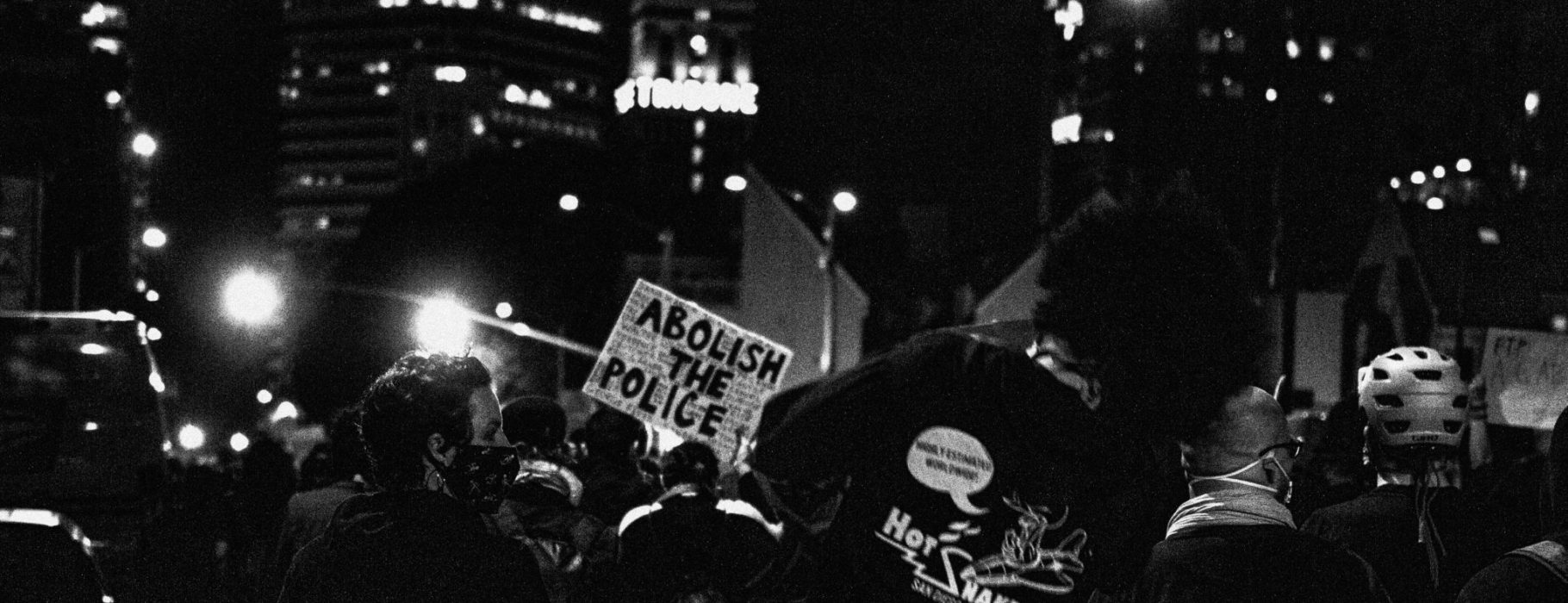 Protesters at night hold signs reading, "Abolish the Police"